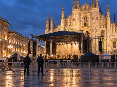 Piazza Duomo a Milano di sera con il palco in allestimento e le transenne per i controlli di sicurezza